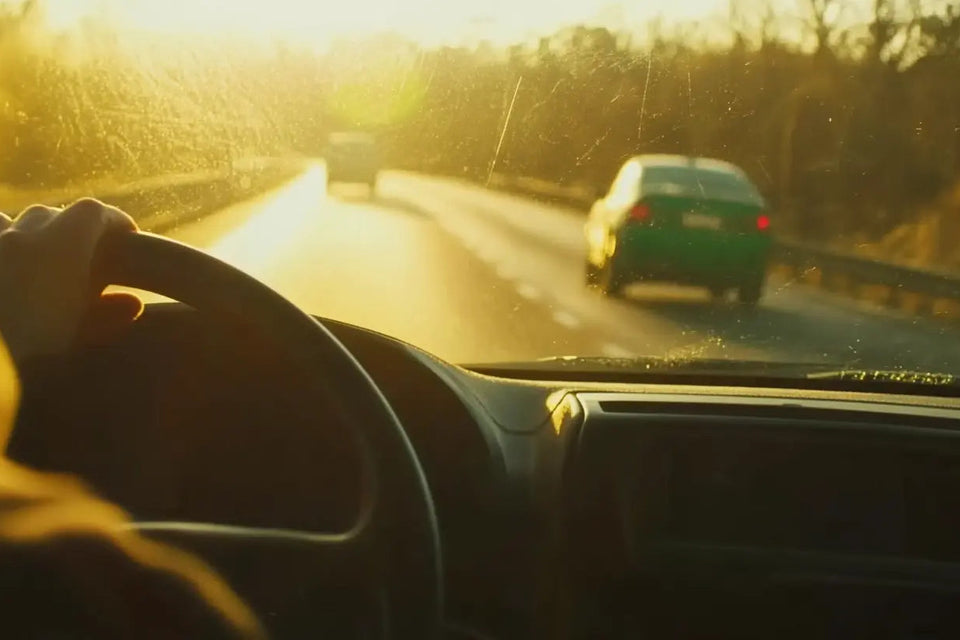Intérieur réaliste d’une voiture au coucher du soleil, mains sur le volant, ambiance chaleureuse et calme avec une fiole de CBD visible dans le porte-gobelet, symbolisant la conduite responsable.