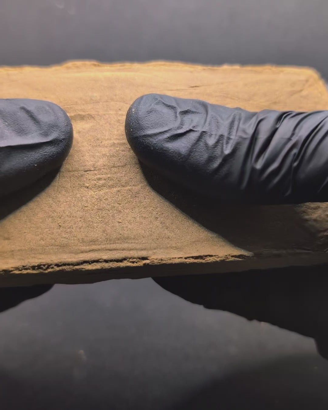 Gros plan sur la résine CBD Peach Indoor Premium tenue avec des gants noirs, montrant sa texture fine et sa qualité indoor supérieure.